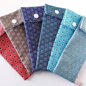 Könnte beinhalten: Sechs Stoffetuis in verschiedenen Farben, darunter Rot, Braun und Blautöne. Jedes Etui hat ein geometrisches Sternmuster und einen weißen Knopfverschluss. Die Etuis sind wahrscheinlich für die Aufbewahrung kleiner Gegenstände gedacht.