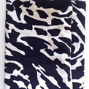 May include: Folded fabric with a striking black and white pattern. The design features irregular, organic shapes, similar to animal print. The fabric appears smooth, possibly silk or a similar material. The overall aesthetic is modern and eye-catching.