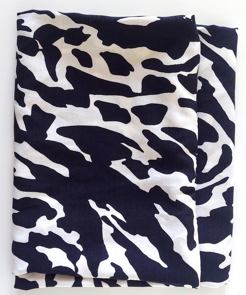 May include: Folded fabric with a striking black and white pattern. The design features irregular, organic shapes, similar to animal print. The fabric appears smooth, possibly silk or a similar material. The overall aesthetic is modern and eye-catching.