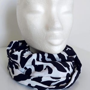 May include: An infinity scarf with a black and white abstract pattern. The scarf is draped around a white mannequin head. The design features black shapes on a white backdrop. The fabric appears to be soft and lightweight, suitable for cooler weather.