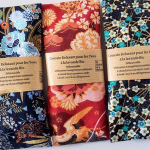 May include: Three eye pillows with floral designs. One is navy blue with white and light blue flowers, another is red with orange and white flowers, and the third is black with teal and gold flowers. Each pillow has a brown label with French text.