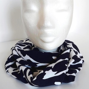 May include: A black and white patterned infinity scarf, displayed on a mannequin head. The scarf features a striking abstract design. The fabric appears soft and drapes well, suitable for various outfits and styles.