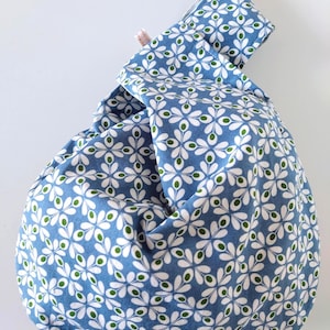 May include: A blue fabric knot bag with a white and green floral pattern. The bag is made of soft material and has a unique knot closure. The bag is a stylish accessory for carrying small items.