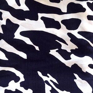 May include: A close-up shot of a fabric with a striking abstract design. The pattern consists of large, navy blue shapes set against a white backdrop. The texture of the fabric is evident, indicating a soft material, possibly for clothing or home furnishings.
