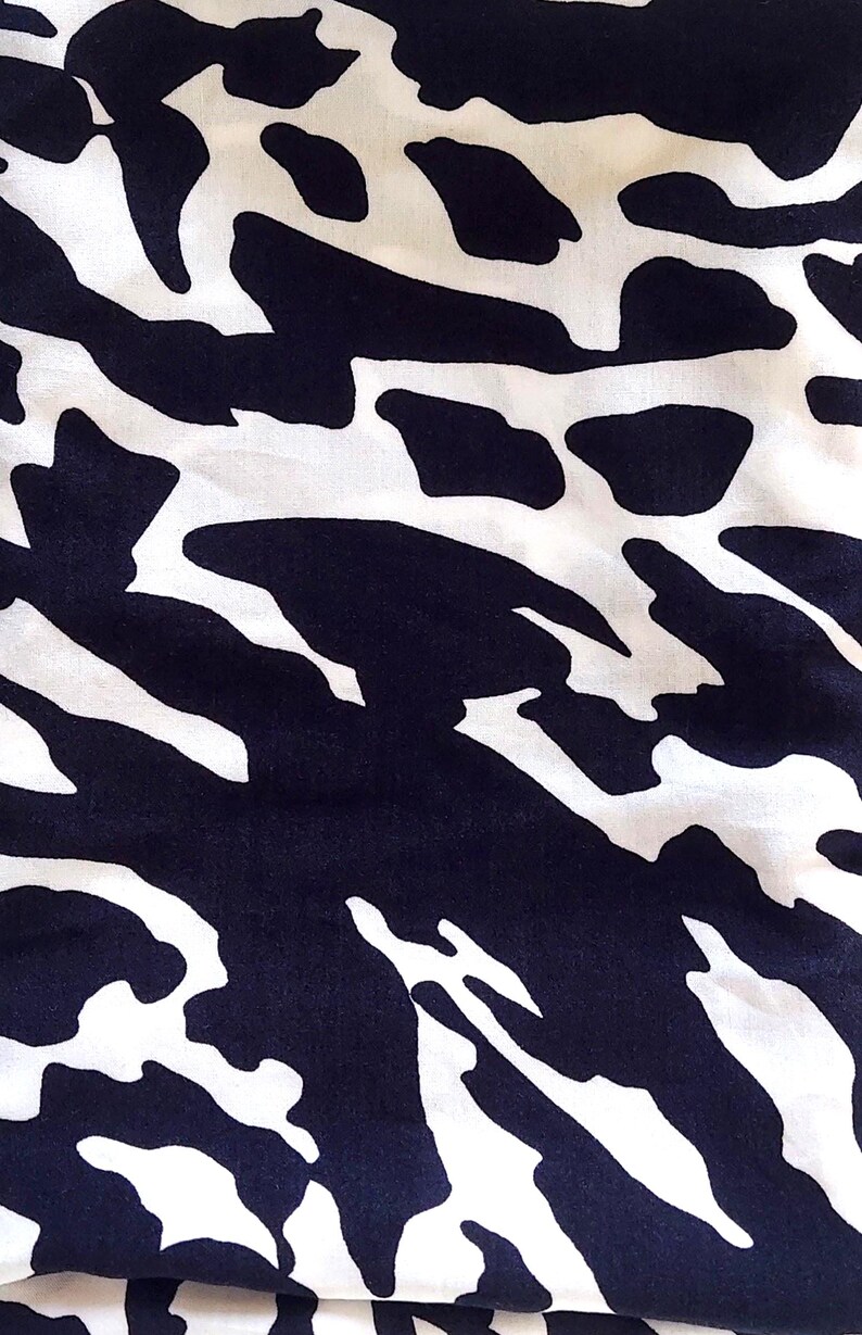May include: A close-up shot of a fabric with a striking abstract design. The pattern consists of large, navy blue shapes set against a white backdrop. The texture of the fabric is evident, indicating a soft material, possibly for clothing or home furnishings.