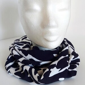 May include: A navy and white patterned infinity scarf, displayed on a mannequin head. The scarf's design features irregular white shapes against a dark blue backdrop. The fabric appears soft and drapes well, suggesting a comfortable accessory.