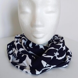 May include: A navy and white infinity scarf with a repeating abstract pattern. The scarf is draped around a white mannequin head. The pattern is a bold, contrasting design.