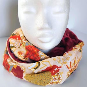May include: A reversible infinity scarf with a floral pattern in red, gold, and cream on one side and a deep burgundy plush fabric on the other. The scarf is wrapped around a white mannequin head.