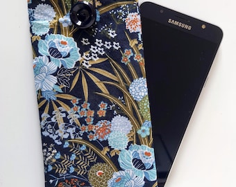 May include: A rectangular fabric phone pouch featuring a dark navy blue background with a floral pattern of light blue, white, and orange flowers and green leaves. The pouch has a black button closure with an elastic loop and a black Samsung smartphone.