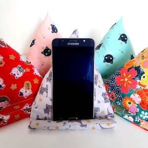 Peut inclure: Un smartphone est présenté dans un support de téléphone en tissu. Le support est entouré d'oreillers triangulaires en tissu coloré avec des motifs de chats et de fleurs. Les oreillers sont rouges, roses, turquoise et à motifs japonais.