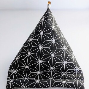 May include: A black and white geometric patterned triangular pillow. The pillow features a repeating starburst design in white against a black background. A small gold-colored clip is attached to the top of the pillow.