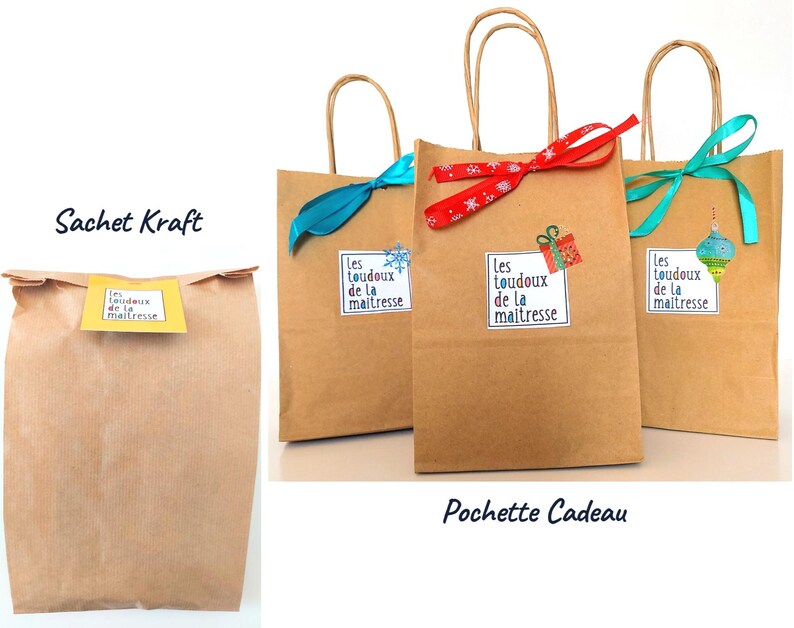 May include: Kraft paper gift bags with paper handles. The bags are decorated with ribbons and stickers. The stickers have the text "Les toudoux de la maitresse". One bag has a blue ribbon, one has a red ribbon, and one has a teal ribbon.