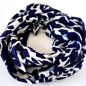 May include: A navy and white patterned infinity scarf. The scarf is a continuous loop, featuring a repeating design of white, organic shapes against a dark blue backdrop. The fabric appears soft and drapes well, suitable for various styles.