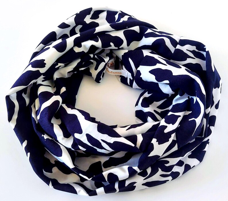 May include: A navy and white patterned infinity scarf. The scarf is a continuous loop, featuring a repeating design of white, organic shapes against a dark blue backdrop. The fabric appears soft and drapes well, suitable for various styles.