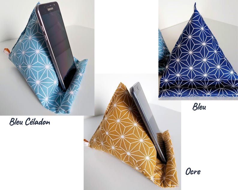 May include: Triangle-shaped fabric phone stands in blue, navy, and ochre, each with a white geometric pattern. A smartphone rests in each stand, showcasing the product's functionality. The stands are labeled "Bleu C&eacute;ladon", "Bleu", and "Ocre".