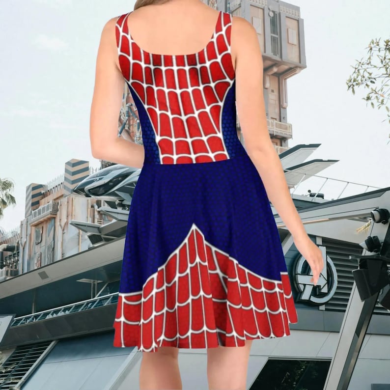 A woman wearing a dress with a spider web pattern on it, standing in front of a building with a futuristic design.