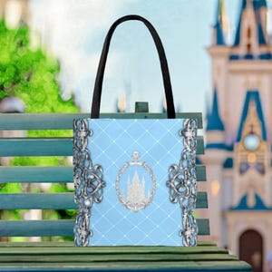 A blue tote bag with a castle-like design and a castle silhouette on it, placed on a green bench.