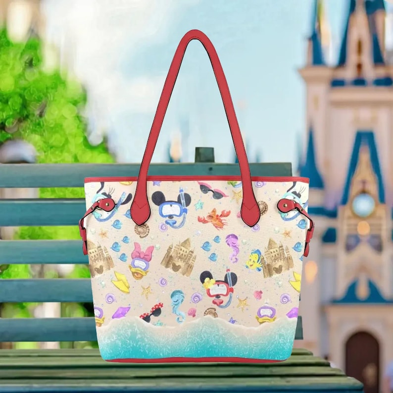 A colorful tote bag with a beach-themed design, featuring various cartoon characters and sea-themed elements such as a mermaid, a castle, and a mermaid tail.