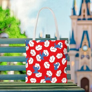 A red tote bag with a pattern of white and blue leaves is displayed on a green bench, with a castle visible in the background.