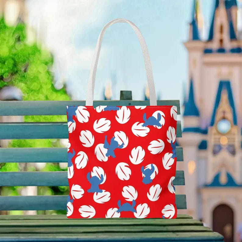 A red tote bag with a pattern of white and blue leaves is displayed on a green bench, with a castle visible in the background.