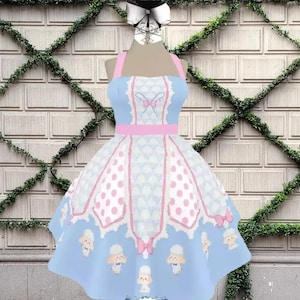 May include: A light blue sleeveless dress featuring a white scalloped pattern, pink polka dot panels, and a pink waist band. The skirt displays a repeating print of small white sheep with blue bows. The bodice includes a central pink bow detail.