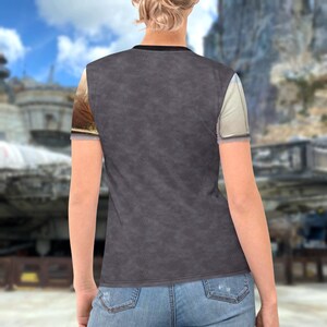 a person wearing a gray t-shirt with a graphic design on the left side, standing in front of a cityscape with buildings and a bridge in the background.