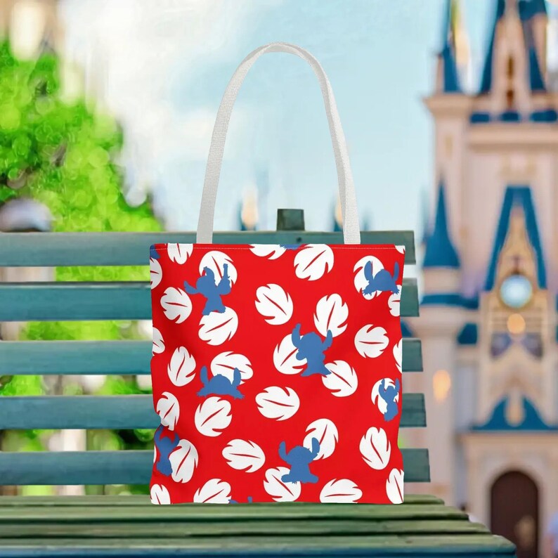 A red tote bag with a white handle and a pattern of white and blue leaves is displayed on a green bench.
