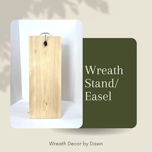 May include: A light-colored wooden wreath stand with a metal handle and a black accent. The stand is rectangular and features visible wood grain. Text on the right reads "Wreath Stand/ Easel" and "Wreath Decor by Dawn".