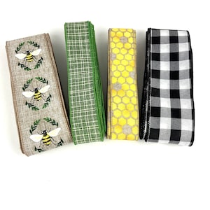 May include: Four different patterned ribbon rolls. The first roll is brown with a repeating pattern of bees and green leaves. The second roll is green with a plaid pattern. The third roll is yellow with a honeycomb pattern. The fourth roll is black and white with a checkered pattern.