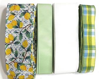 May include: A set of four spools of ribbon arranged side by side. The first features a lemon and green leaf pattern on a white background with blue stars. The second is solid light green, the third is solid white, and the fourth has a yellow, green, and blue plaid pattern.