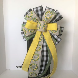 May include: A black lantern with a yellow, green, and black checkered bow. The bow is decorated with a lemon wreath and the text "Hello Sunshine".