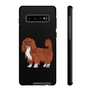 May include: A black phone case featuring a cartoon illustration of a Cavalier King Charles Spaniel dog. The dog is brown and white with a cheerful expression.