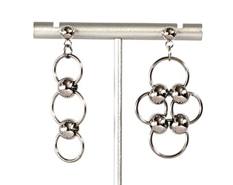 May include: A pair of silver earrings with a geometric design. One earring features a series of connected circles with silver balls, while the other earring has a more intricate design with multiple circles and silver balls.