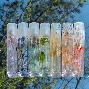 May include: Seven clear glass roller bottles filled with colorful crystals and flowers. The bottles are arranged in a row and are labeled "Freeborn Apothecary".