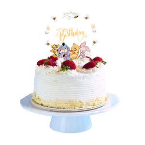 May include: A white cake with whipped cream frosting and strawberries, decorated with a Winnie the Pooh themed cake topper that says "Happy Birthday".