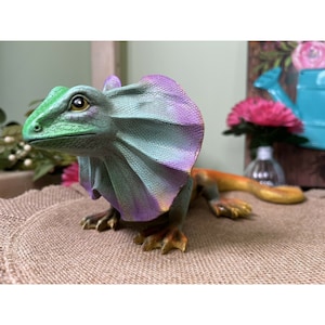 May include: A colorful figurine of a frilled lizard with a green, purple, and orange color scheme. The lizard has a large frill around its neck and is posed in a standing position.