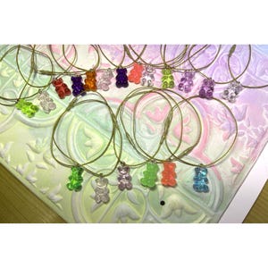 May include: A collection of necklaces featuring translucent gummy bear pendants in various colors including red, orange, yellow, green, blue, purple, and clear, each suspended on a thin, flexible gold-toned wire cord with a metallic clasp.