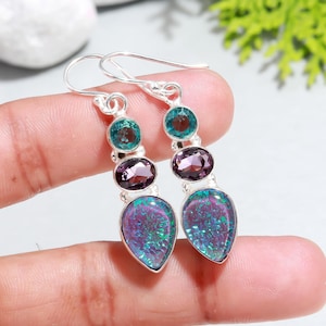 Può includere: Orecchini pendenti in argento con tre pietre preziose. La pietra preziosa inferiore è un'opale iridescente a forma di lacrima, la pietra preziosa centrale è un'ametista rotonda e la pietra preziosa superiore è una pietra rotonda verde.