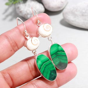 May include: Silver earrings with white spiral pendants and green malachite teardrop stones. The earrings have a hook closure. The malachite stones show a pattern of dark and light green bands.