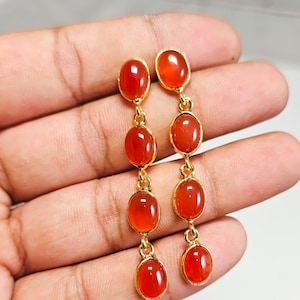 May include: A pair of gold-toned dangle earrings, each featuring four vertically aligned, smooth, oval-shaped orange carnelian gemstones set in metal bezels and connected by small circular jump rings in a linear drop design.