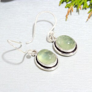 May include: A pair of silver earrings with green gemstone drops. The earrings have a simple, elegant design and are perfect for everyday wear.