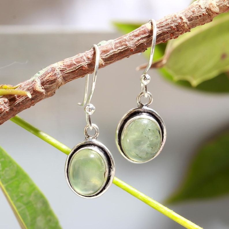 May include: A pair of silver dangle earrings with oval-shaped green gemstones. The earrings have a simple design and are perfect for everyday wear.