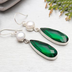 May include: A pair of silver earrings featuring a teardrop-shaped green gemstone and a white pearl accent.