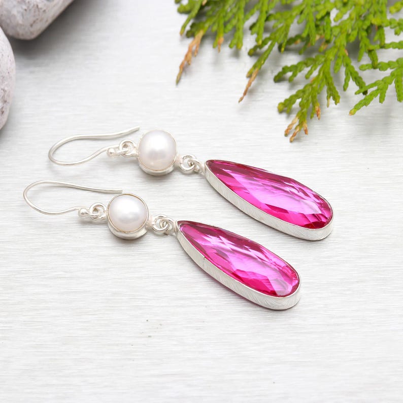 May include: A pair of silver dangle earrings with pink teardrop-shaped gemstones and white pearl accents.