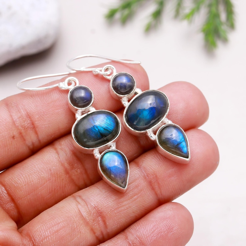 May include: Silver dangle earrings with three iridescent blue labradorite stones. The stones are oval, round, and teardrop shaped.