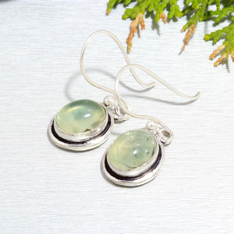May include: A pair of silver earrings with green aventurine stones. The stones are oval shaped and set in a silver bezel. The earrings have a simple hook closure.