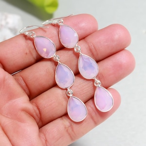 Pode incluir: Brincos pendurados em prata com três pedras preciosas rosa pálido em forma de pêra. Os brincos têm um design delicado e pendurado, com cada gema conectada por um pequeno elo de prata. As pedras preciosas têm uma aparência macia e translúcida.