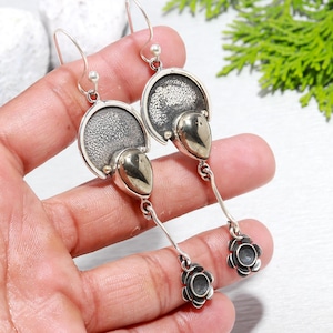 May include: Silver dangle earrings featuring a textured silver disc, a gold-toned teardrop-shaped stone, and a silver flower charm.