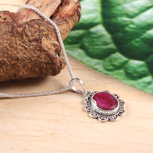 Op de afbeelding: Een zilveren ketting met een hanger met een grote, ovale robijn-edelsteen gezet in een filigrain zilveren ontwerp.