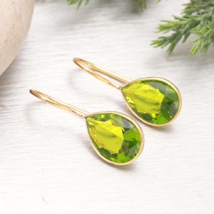 Puede incluir: Un par de pendientes colgantes dorados con piedras preciosas verde claro facetadas en forma de pera. Los pendientes tienen un dise&ntilde;o sencillo y elegante, con las piedras engastadas en un bisel dorado.